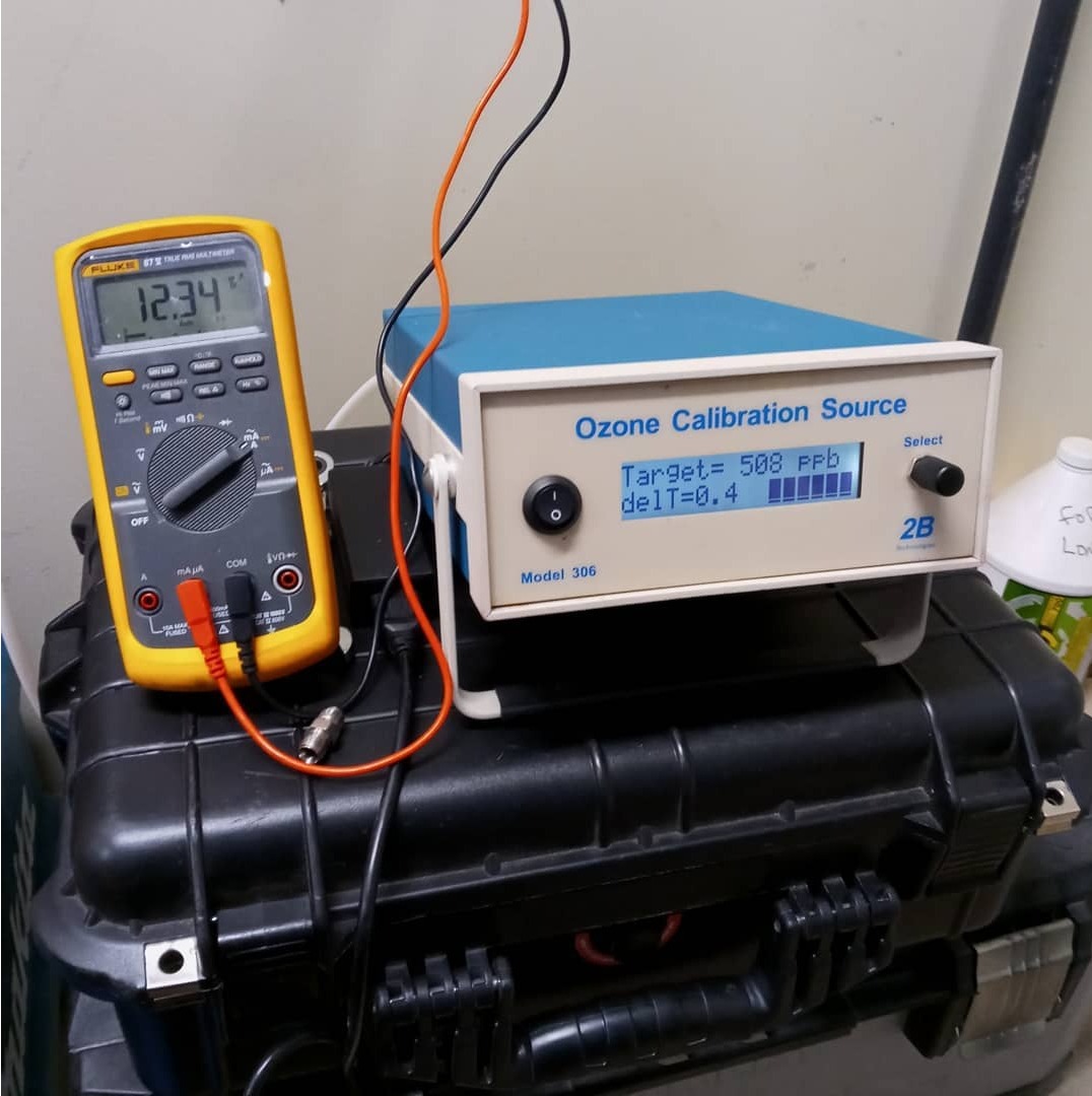 A digital multimeter showing 12.34 and an Ozone Calibration Source device set to 500 ppb on a black carrying case.