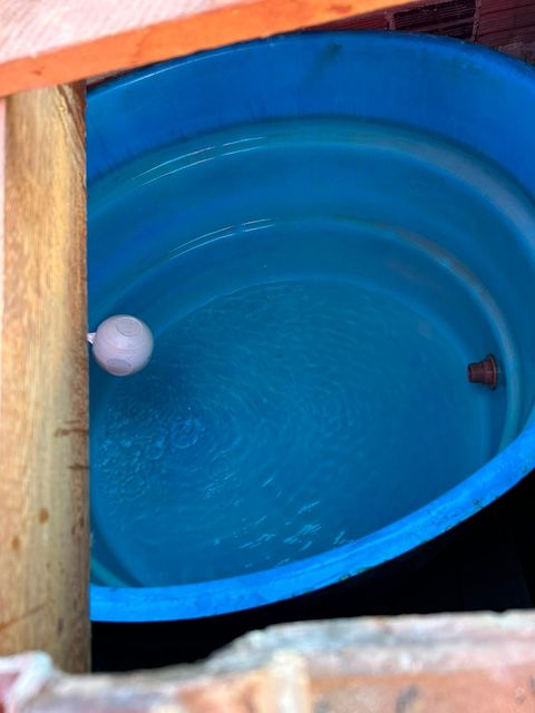 Tanque de plástico azul com uma boia branca e uma pequena peça de metal dentro, visto de cima.