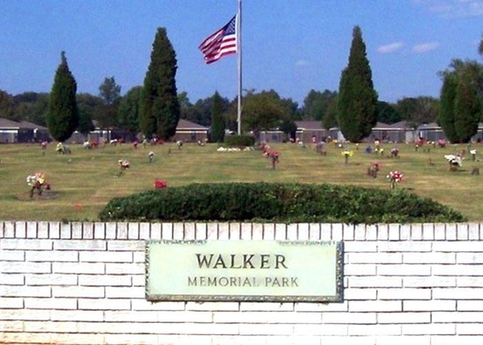 Walker Memorial Park entrance with white brick wall, green sign, grassy field, and American flag in the background