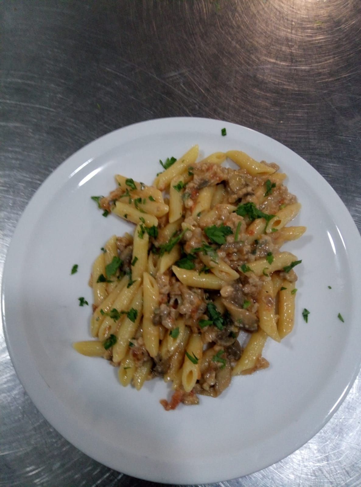 Piatto di pasta con sugo di carne e prezzemolo su un piatto bianco.