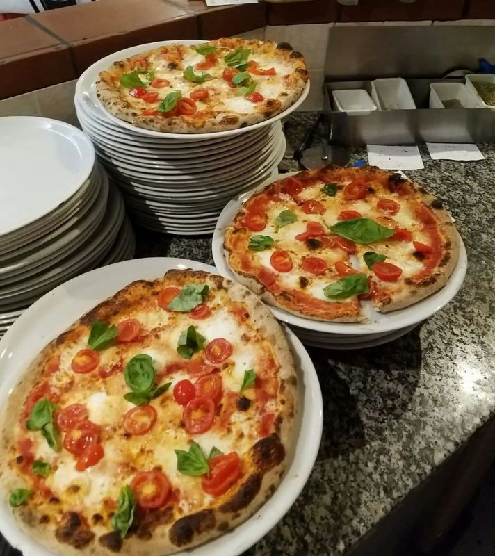 Tre pizze condite con pomodori, basilico e mozzarella, su piatti bianchi, impilati e appoggiati su un bancone.