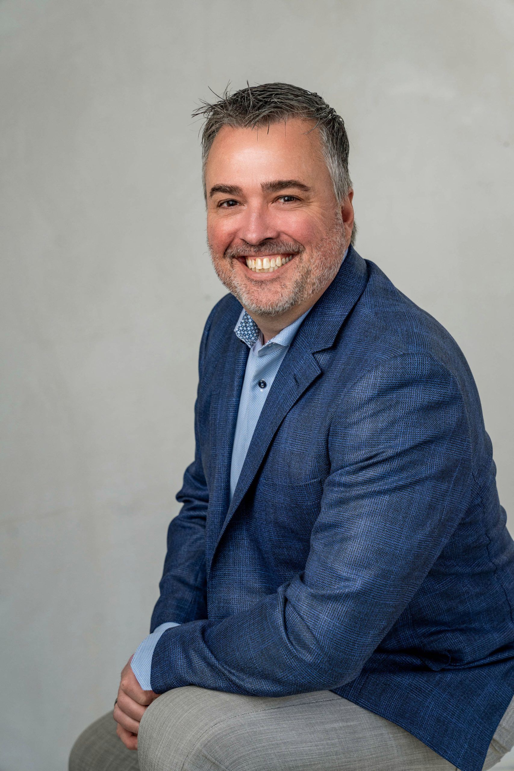 Smiling man in a blue blazer seated against a light gray background