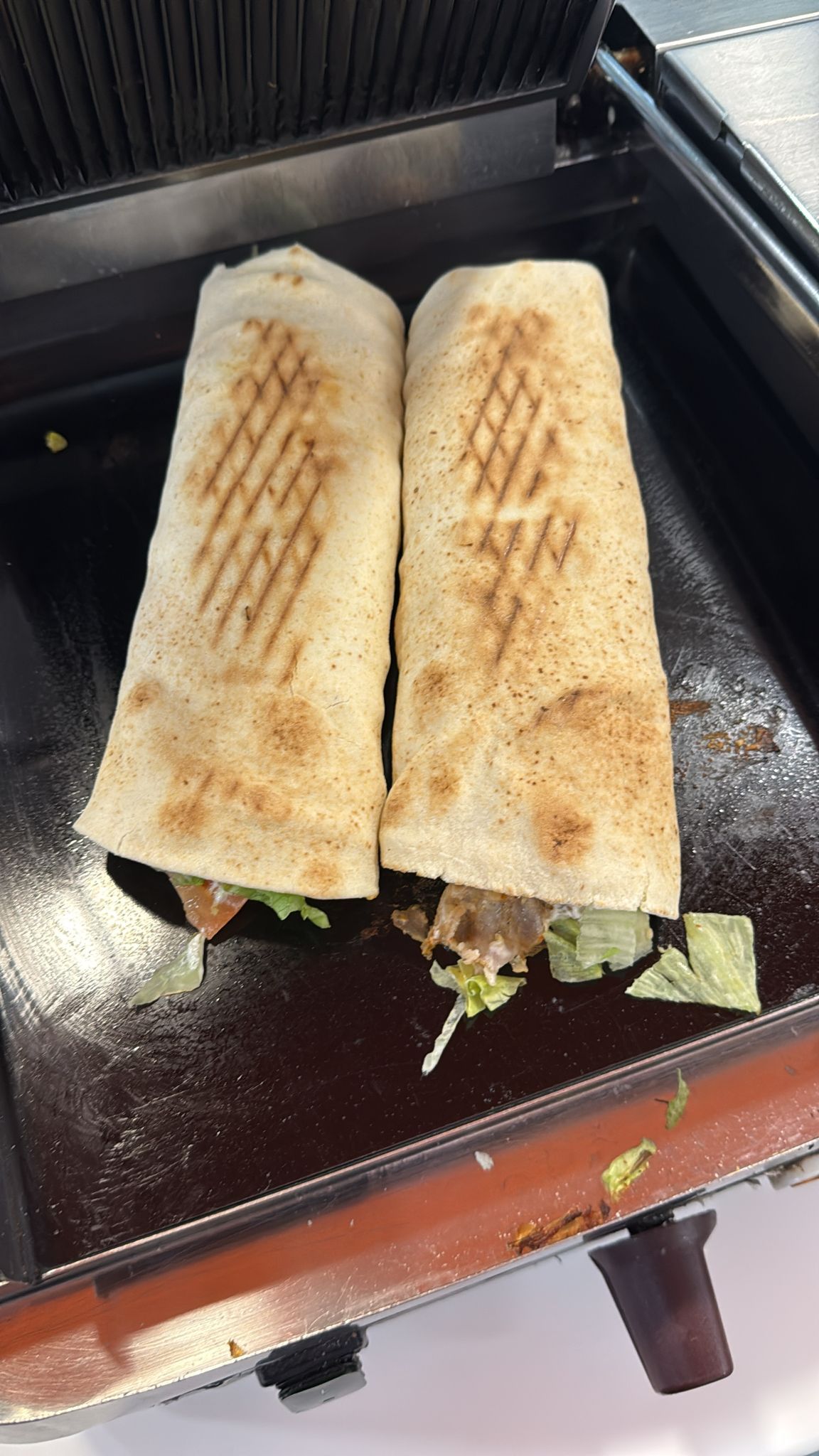 Due panini avvolti, con i segni della griglia, tostati su una piastra per panini nera.