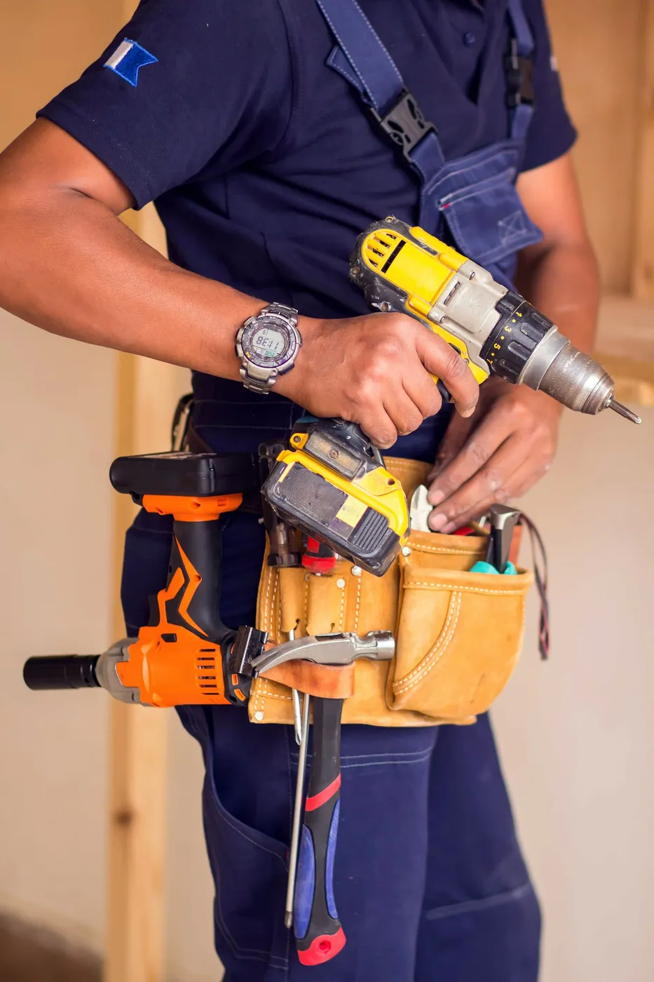 A man is holding a drill and wearing a tool belt.