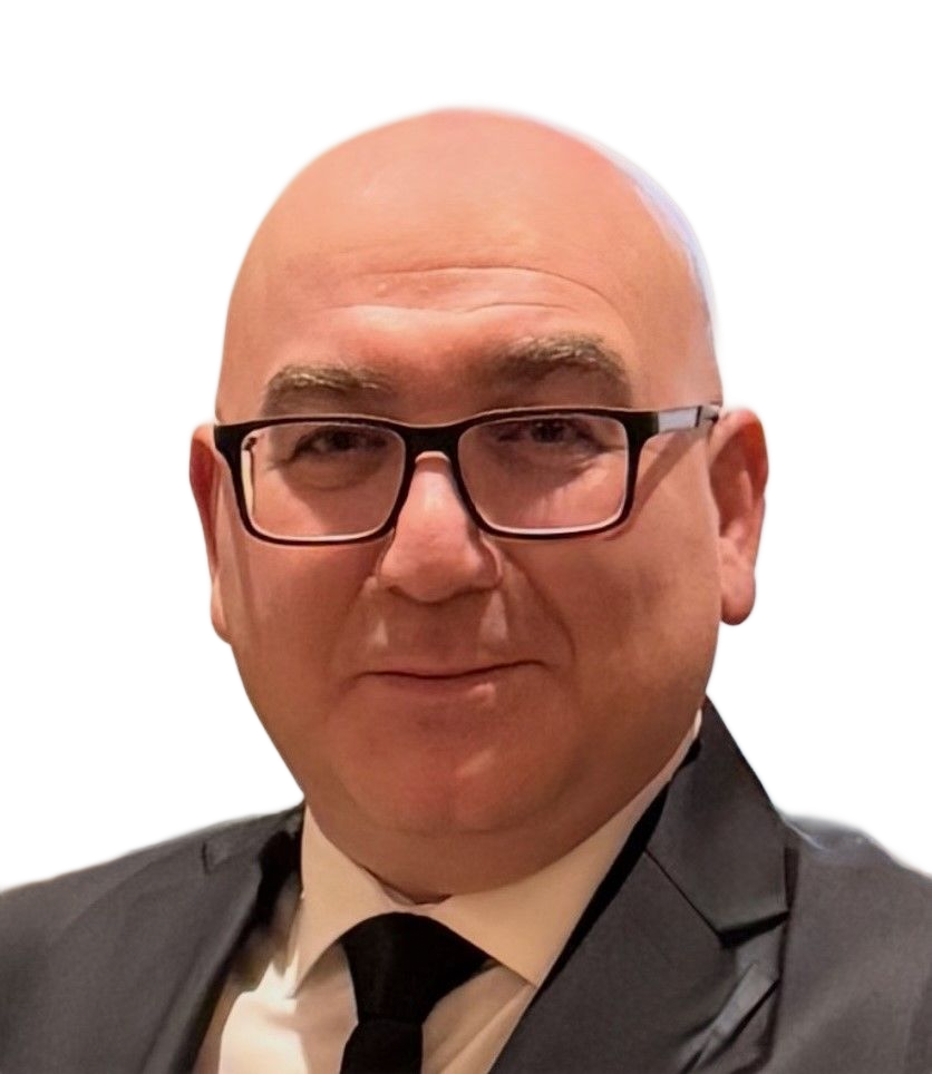 A bald person with glasses wearing a black suit and tie, smiling slightly against a neutral background.