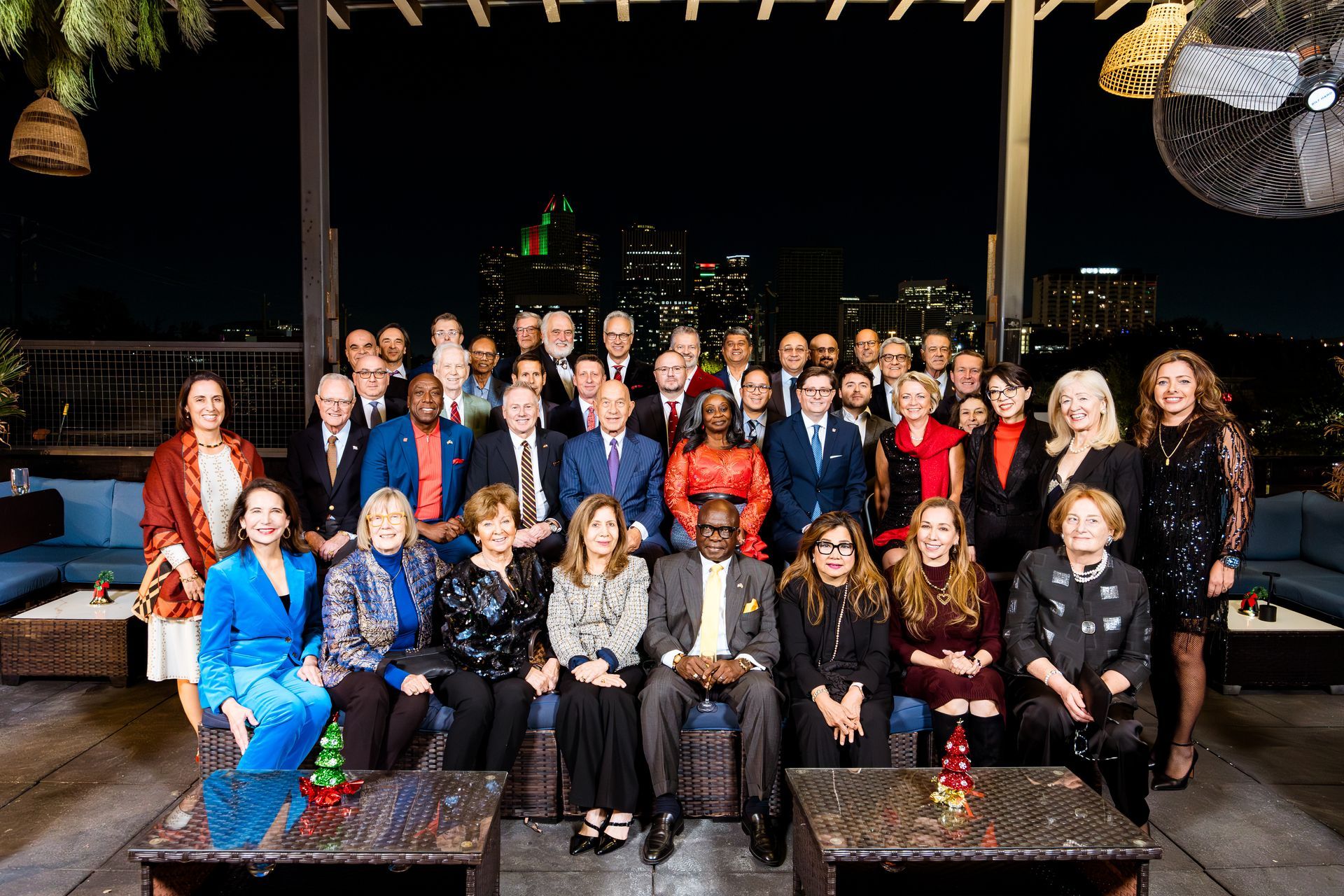 Group of people posing for a formal photo at an outdoor evening event with city lights in the background