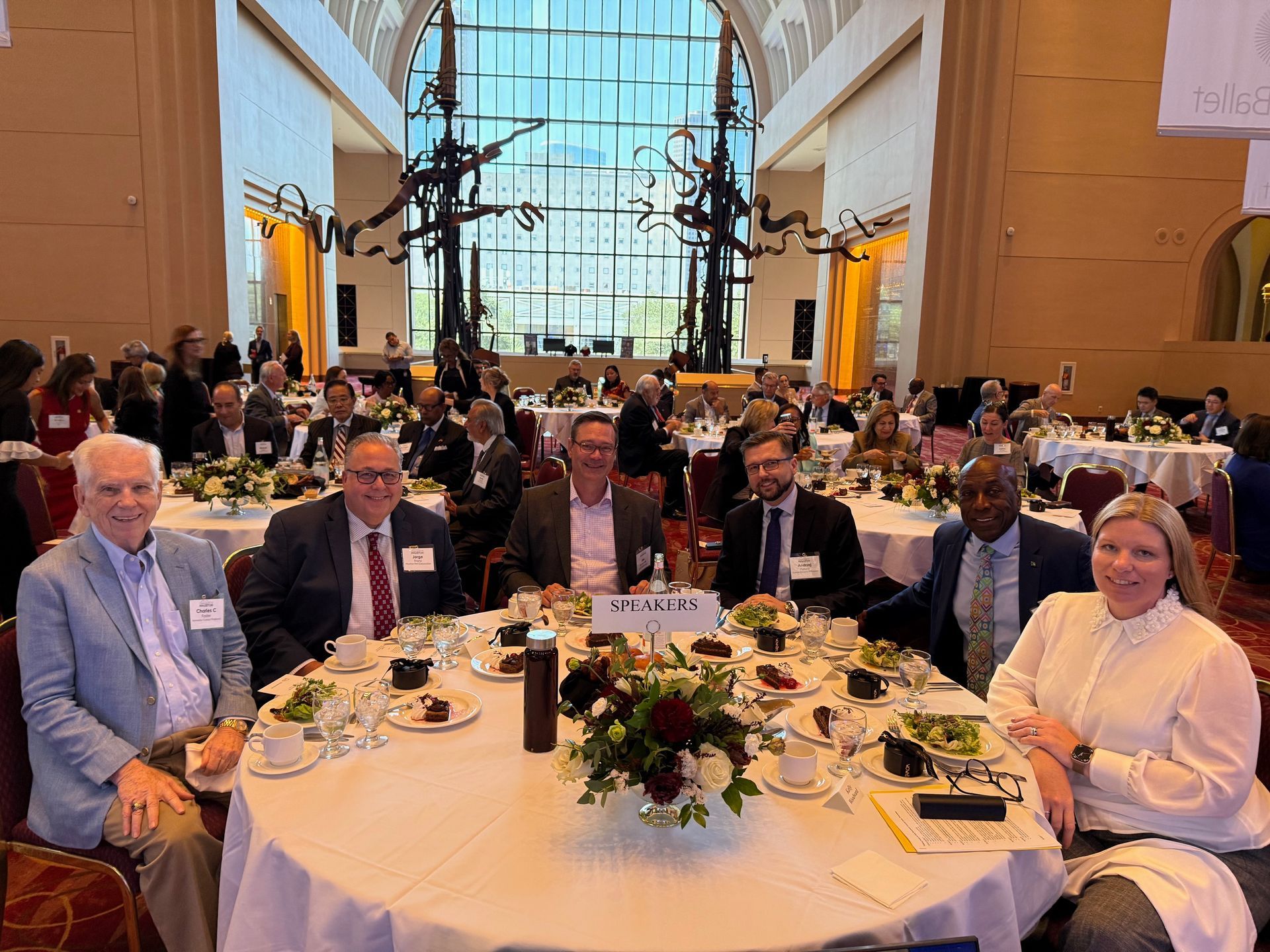 Five professionals sit around a circular table at a conference, smiling at the camera in a large, brightly lit hall.