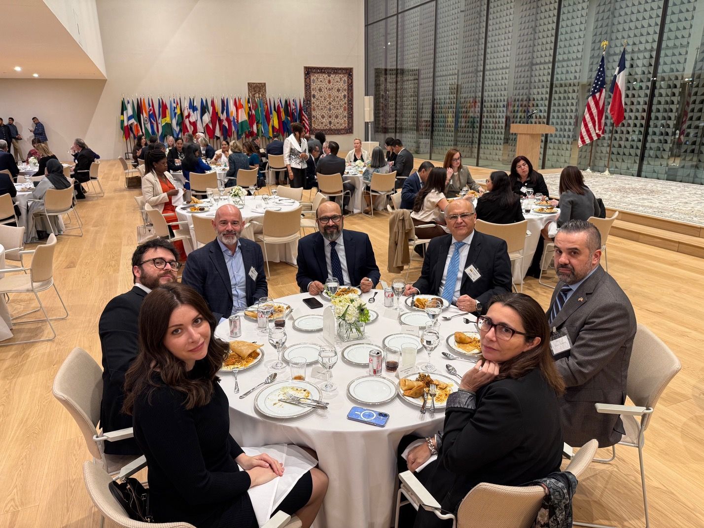 A group of people sitting at a round table for a formal dinner event in a large, modern conference hall.