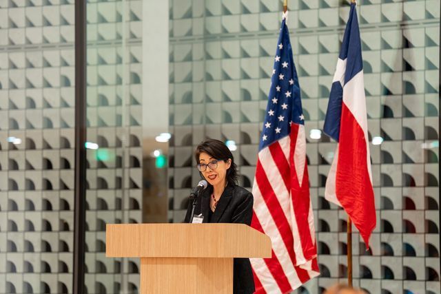 A group sits at a circular dining table in a large, modern hall decorated with international flags in the background.