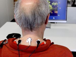 Ein Mann sitzt vor einem Computer. Um seinen Hals sind Kabel befestigt.