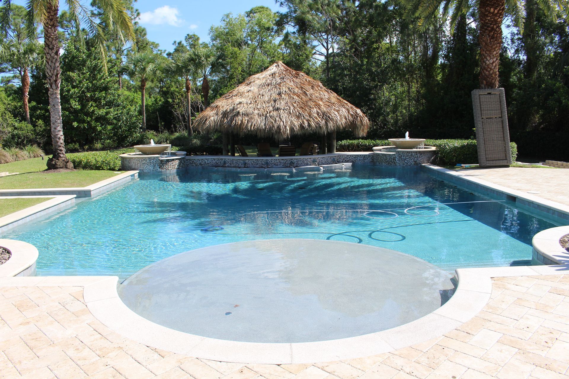 Backyard swimming pool with a thatched-roof cabana and surrounding tropical landscaping