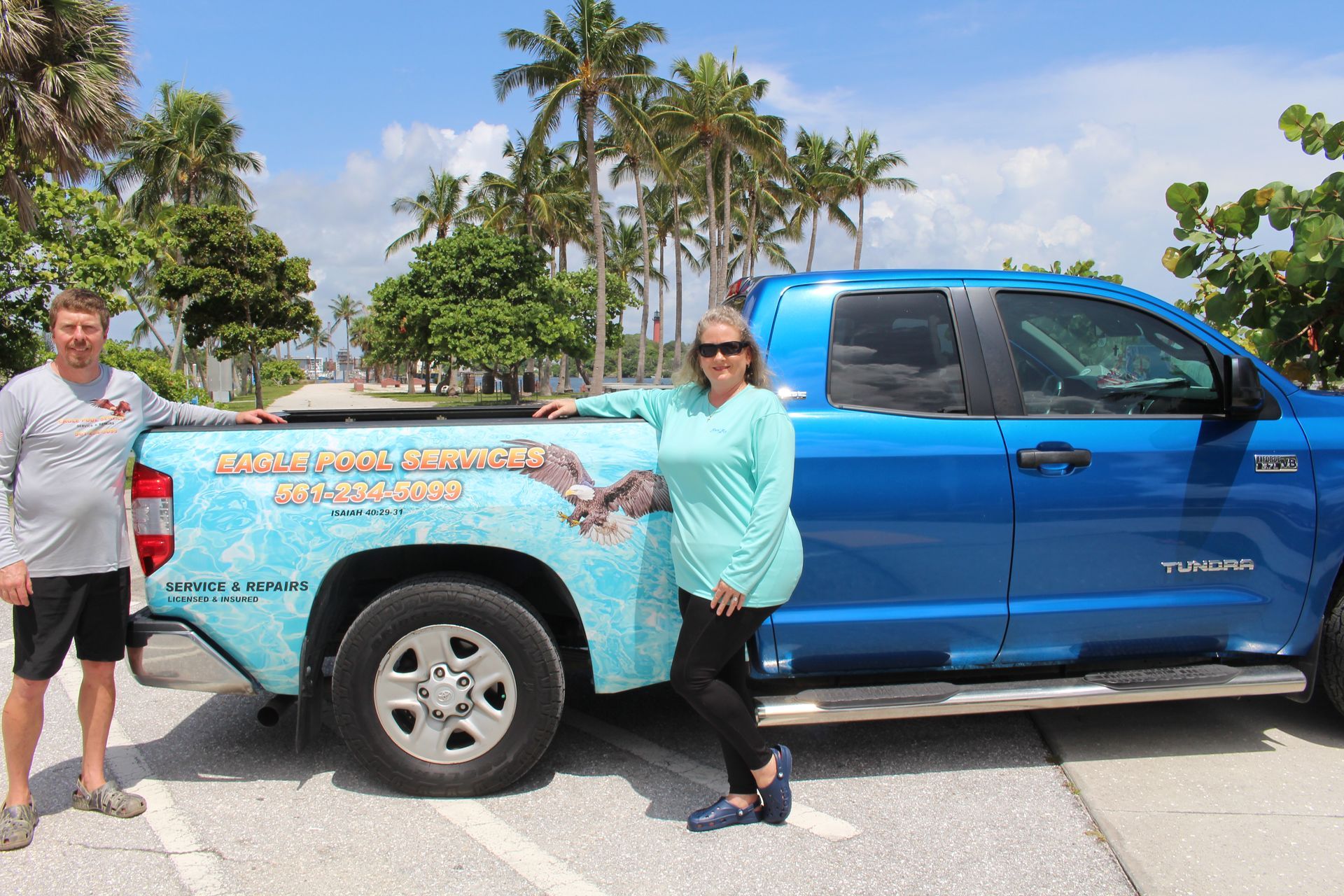 Two people posing beside a blue pickup truck wrapped in a beach map design on a sunny road