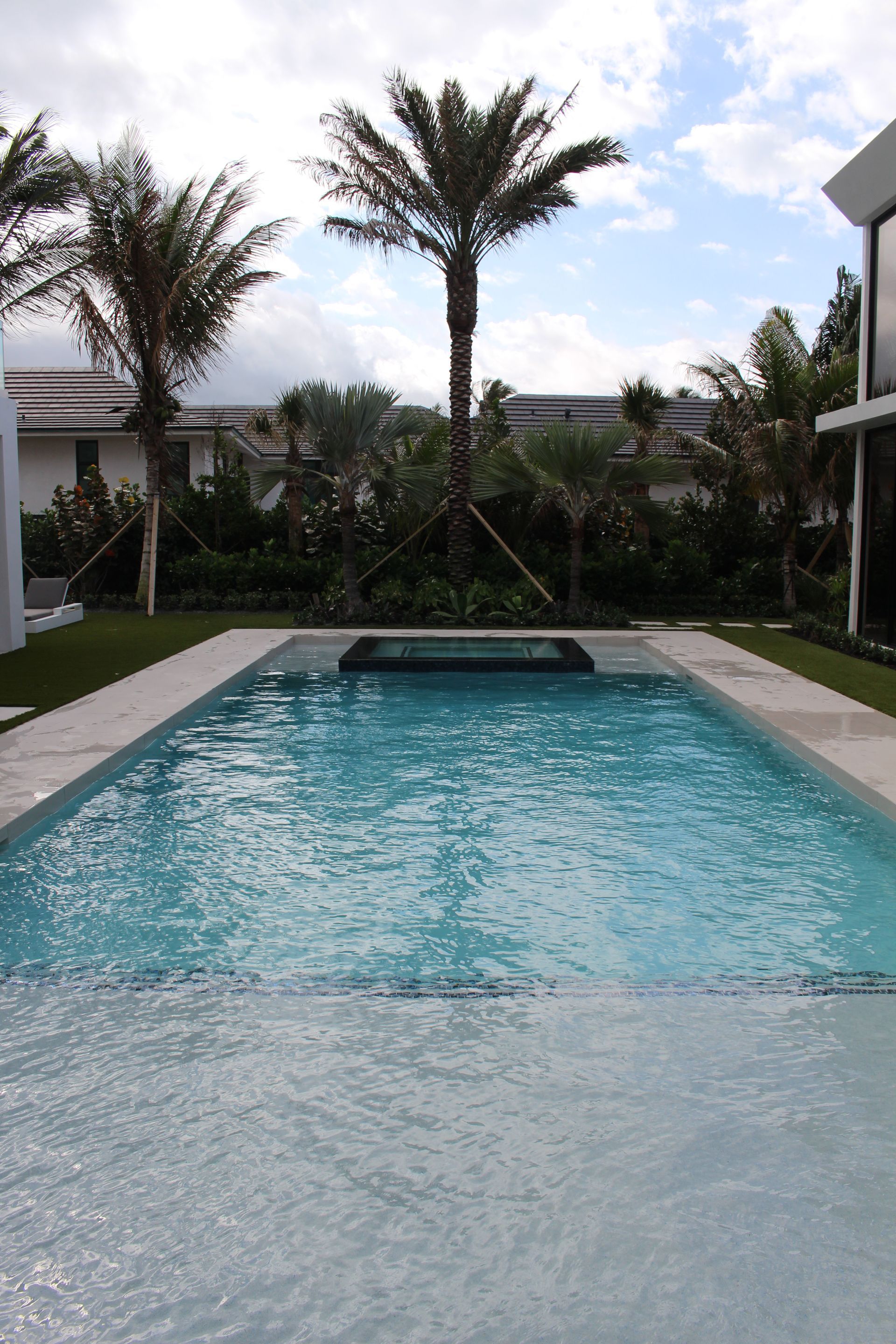 Modern backyard pool with palm trees and a partly cloudy sky