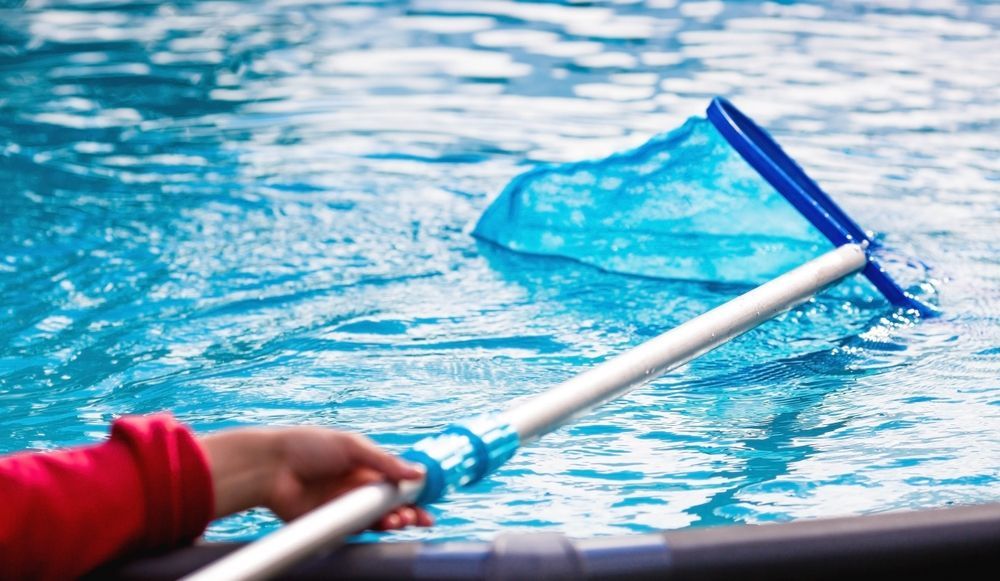 Blue pool skimmer net sweeping debris from water, held by a person in a red sleeve