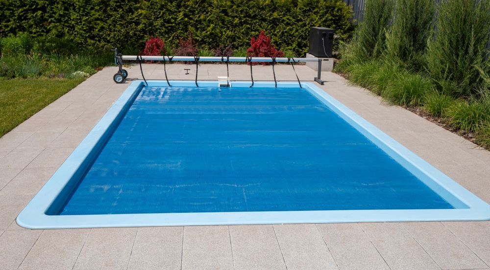 Hand holding a pool tester over blue tiled water with a floating pool thermometer.