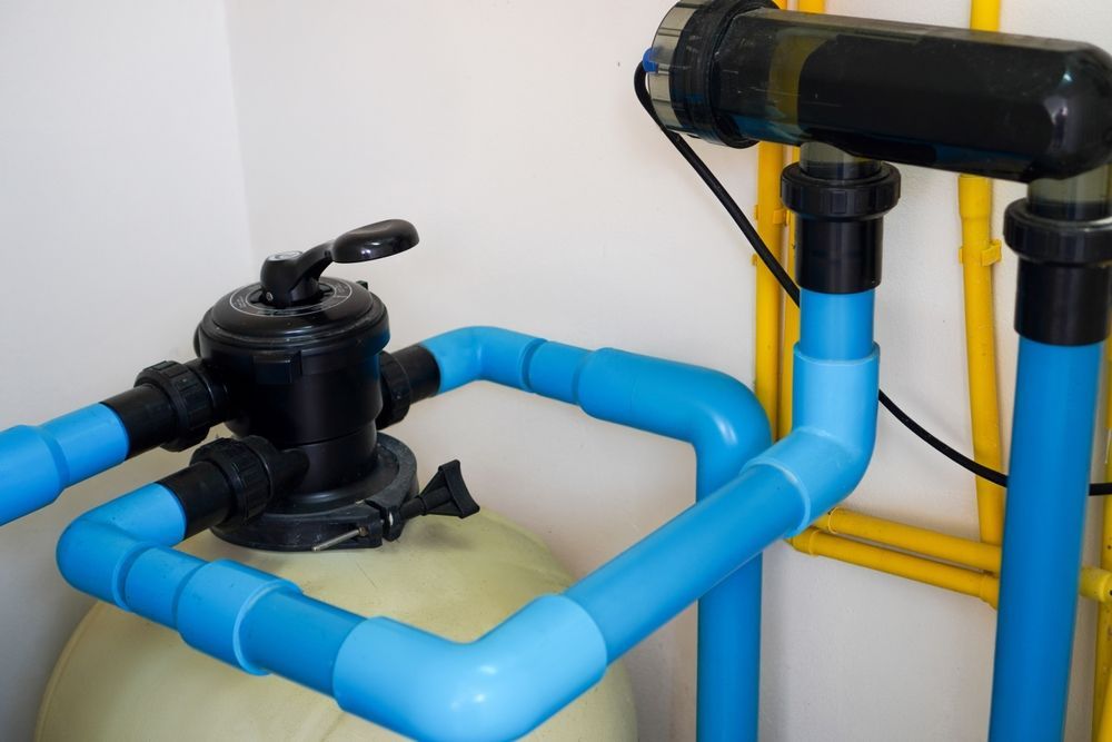 Blue PVC pool piping with a black filter pump and valves beside a wall