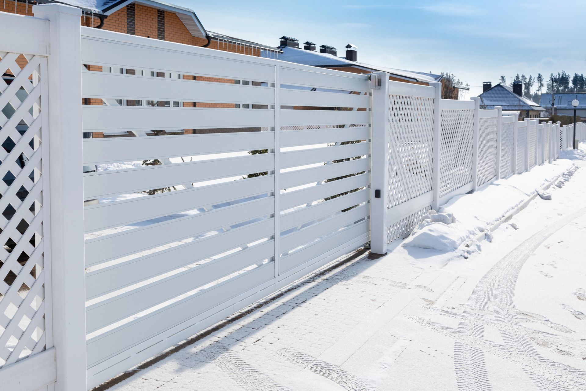 White horizontal slat fence with decorative sections along a snow-covered street.