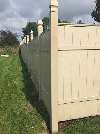 Tan vinyl privacy fence along a green grassy lawn.