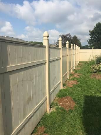 Beige vinyl fence with decorative posts in a grassy Madison, WI yard under a partly cloudy sky.