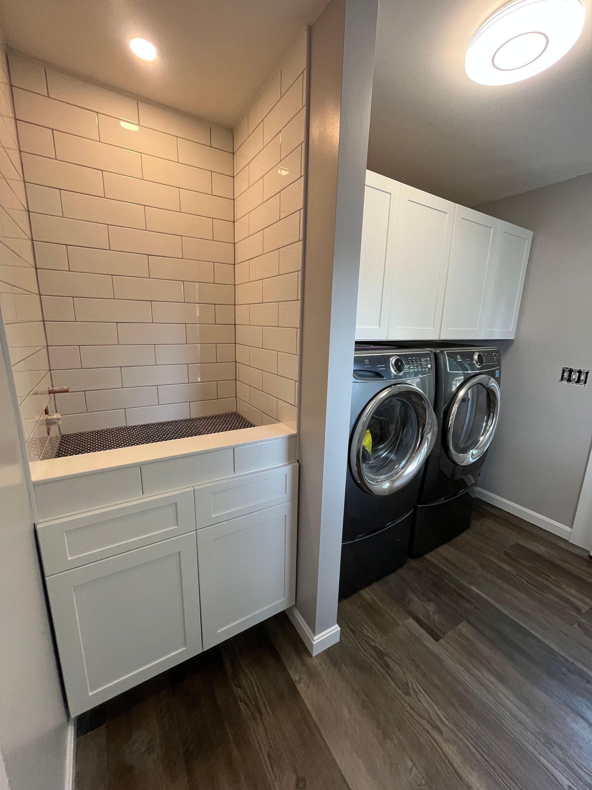 A laundry room with white cabinets, tile backsplash, a pet washing station, and black washer and dryer units.