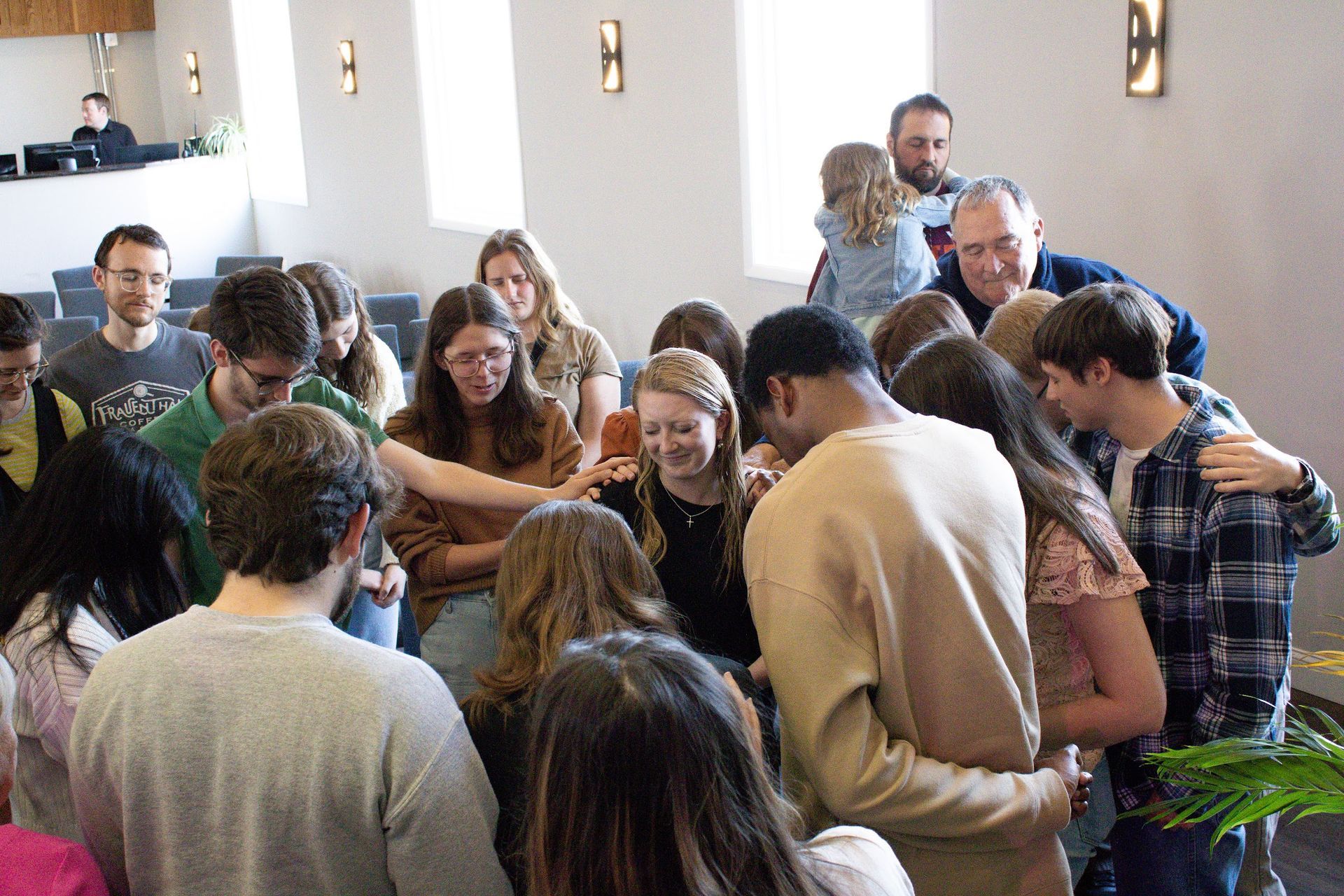 A group of people are standing in a circle with their arms around each other praying