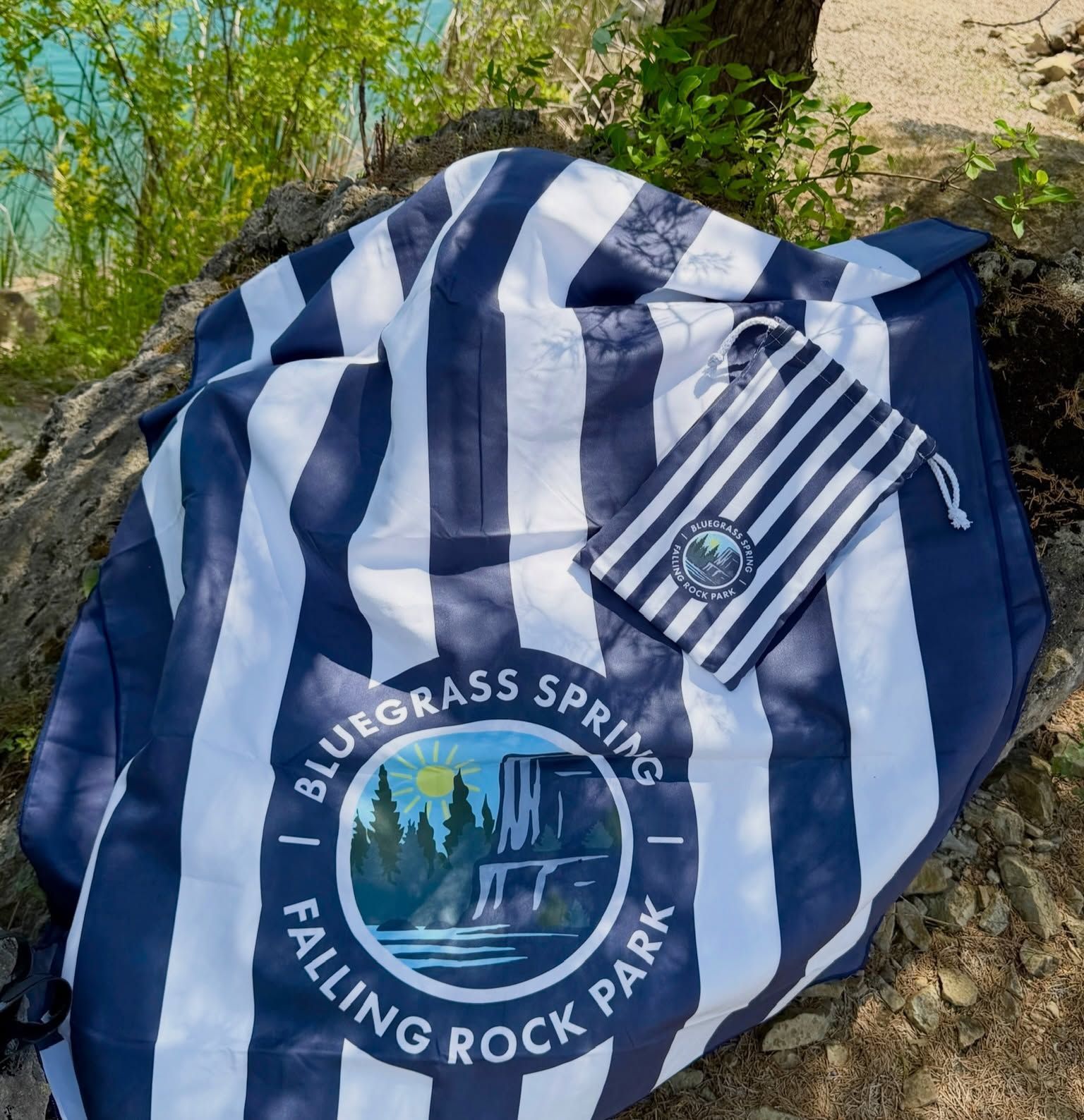 Blue-and-white striped shirt with Bluegrass Springs Falling Rock Park logo on rocks by water