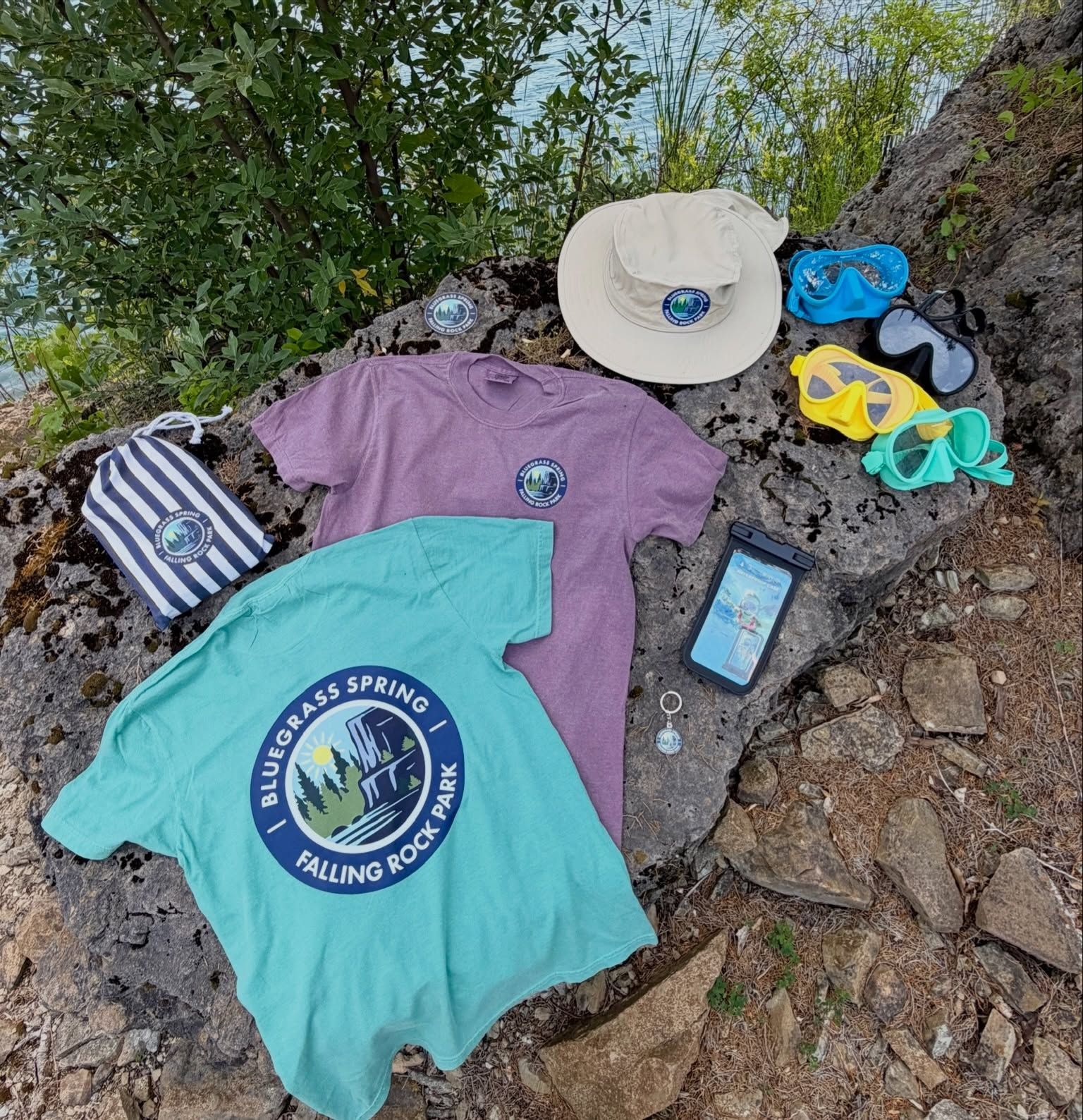 Outdoors on a rock: teal and purple spring hiking shirts, hat, sandals, socks, and a phone.