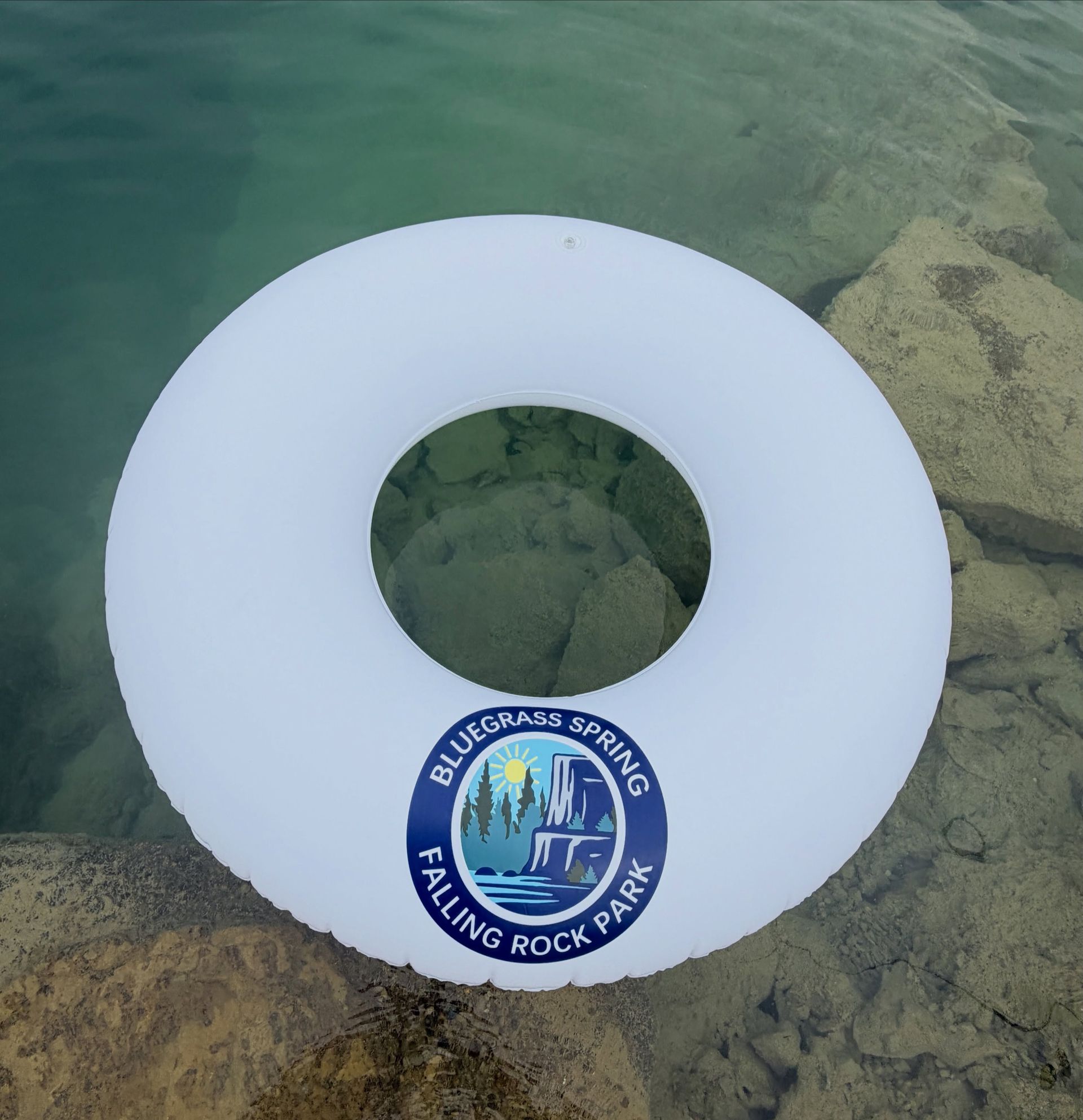 White swim ring floating in clear water over rocks, with a Bluewater Springs Climbing Rock Park sticker.