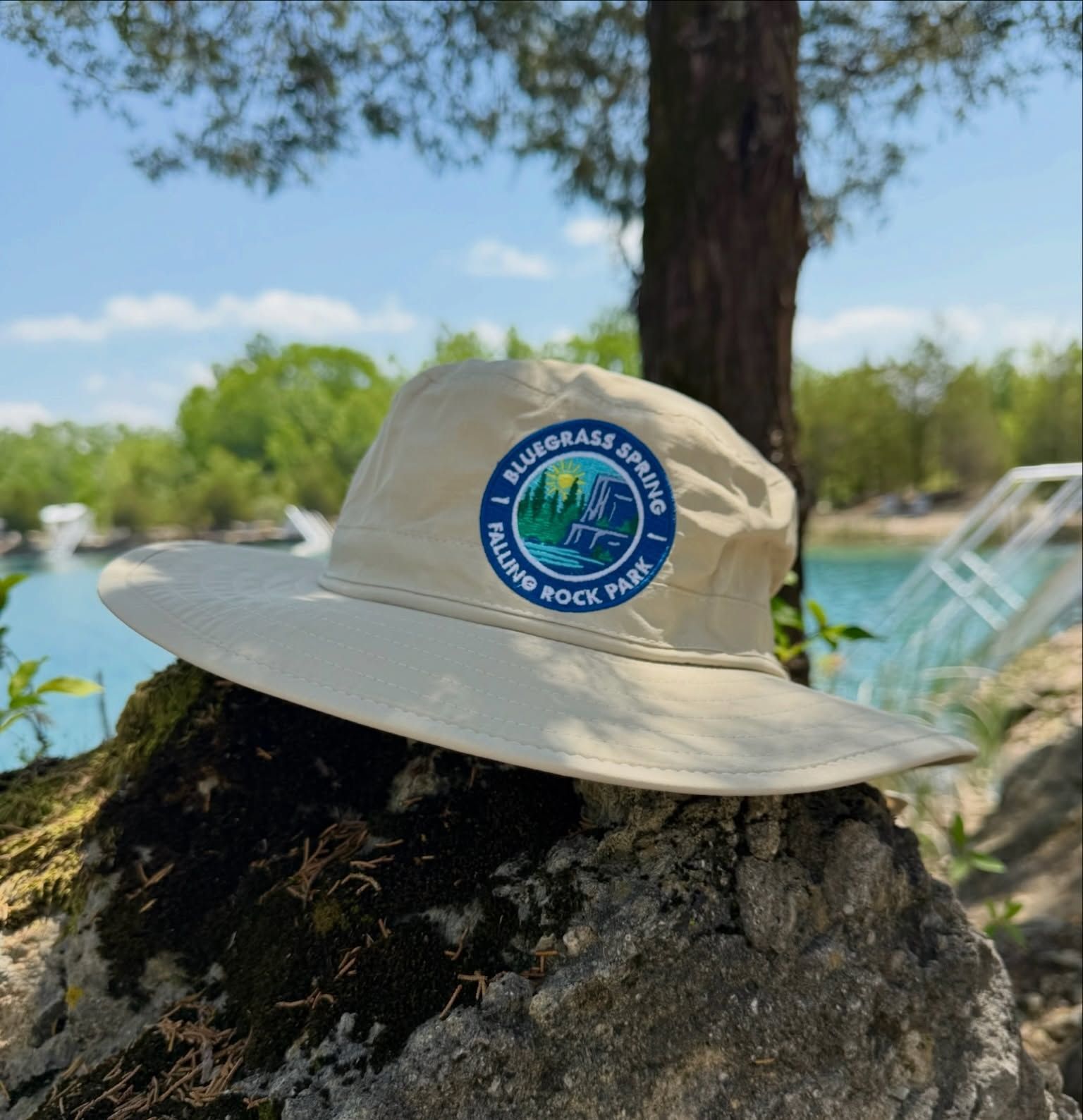 Beige hat with a blue circular patch resting on a tree stump outdoors near water and trees