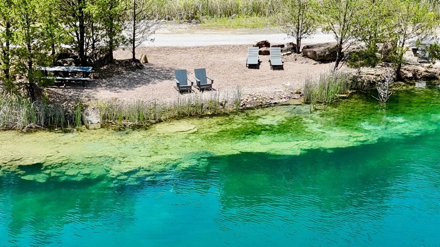 Lakeside beach with turquoise water, sandy shore, and several lounge chairs under trees