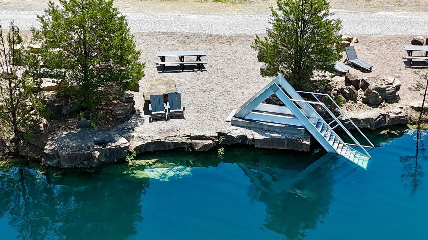 Lakeside dock with blue-roofed boat ramp, picnic tables, trees, and turquoise water below