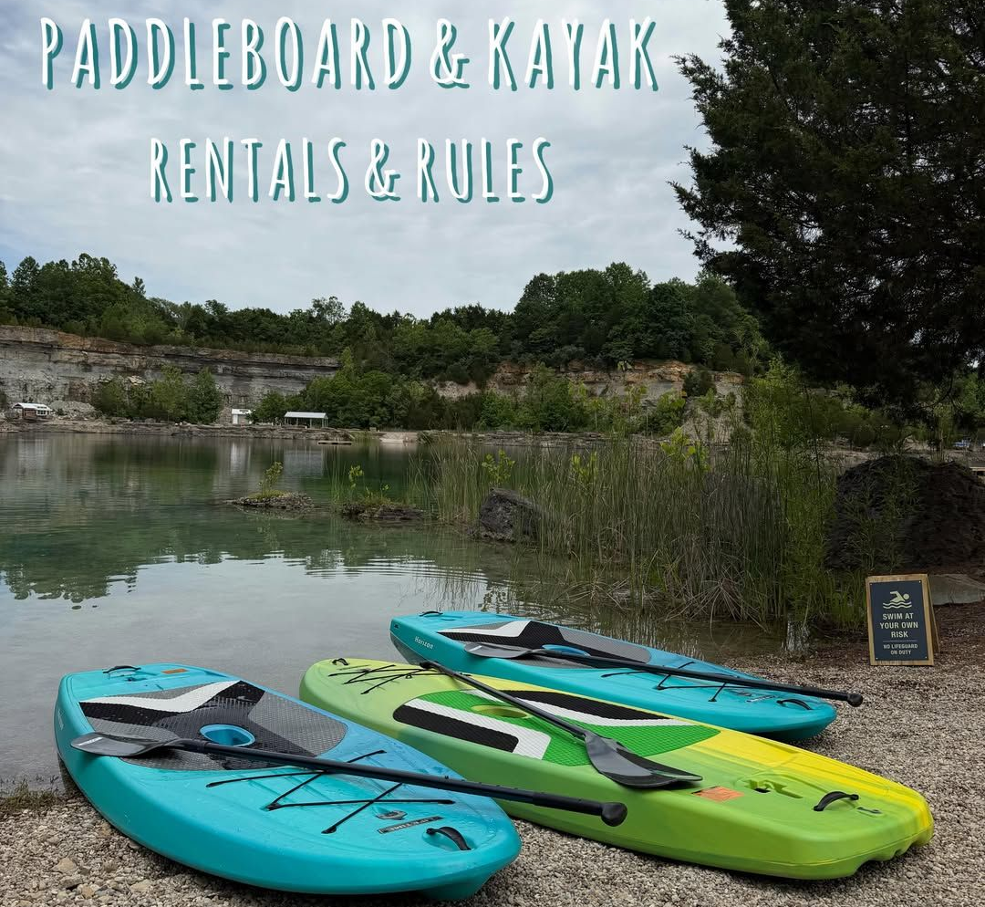 Paddleboard and kayak rentals sign beside three colorful boards by a calm lake shore