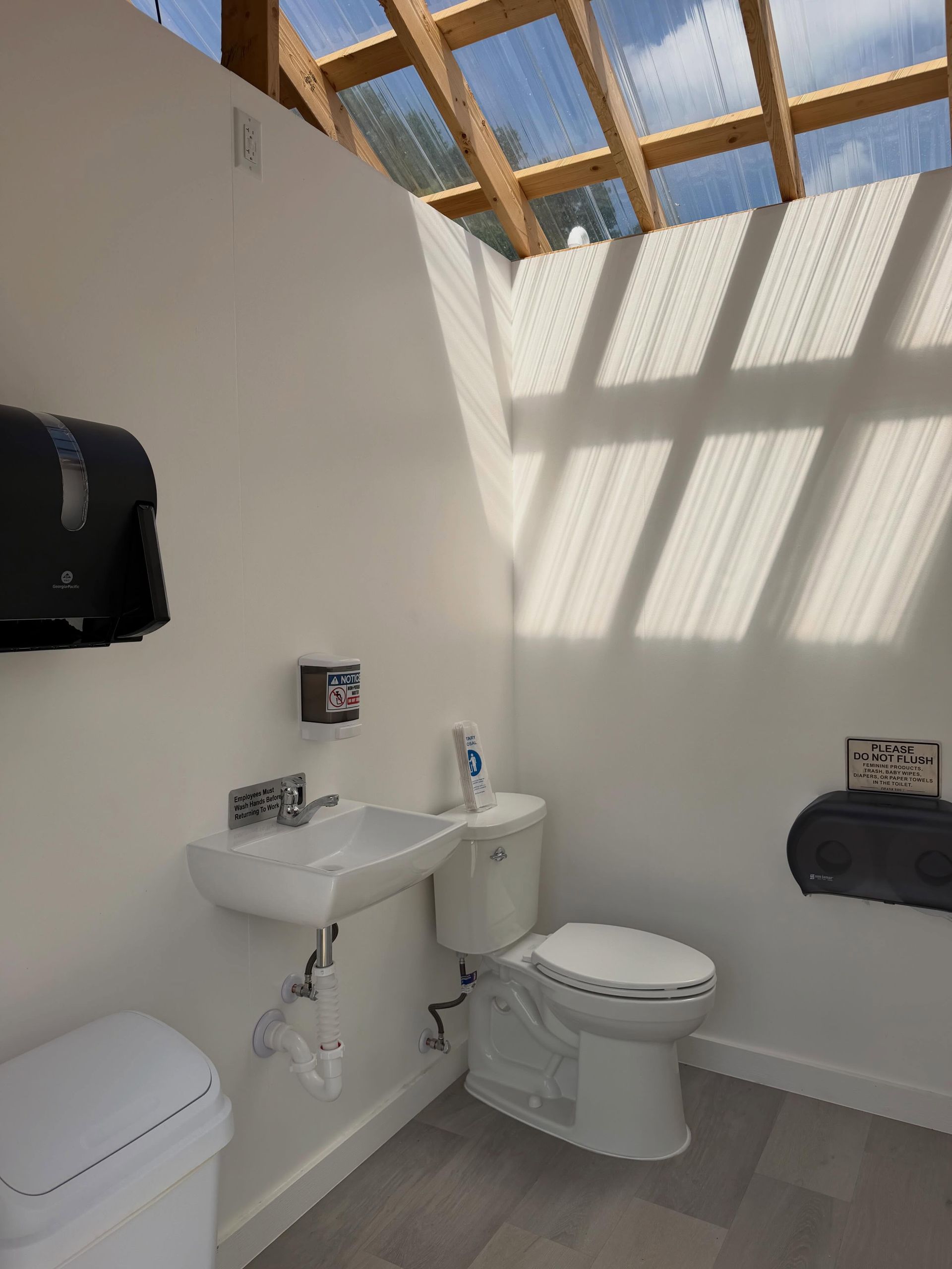 Small bathroom with toilet, sink, paper dispenser, and skylight casting shadows on white walls.
