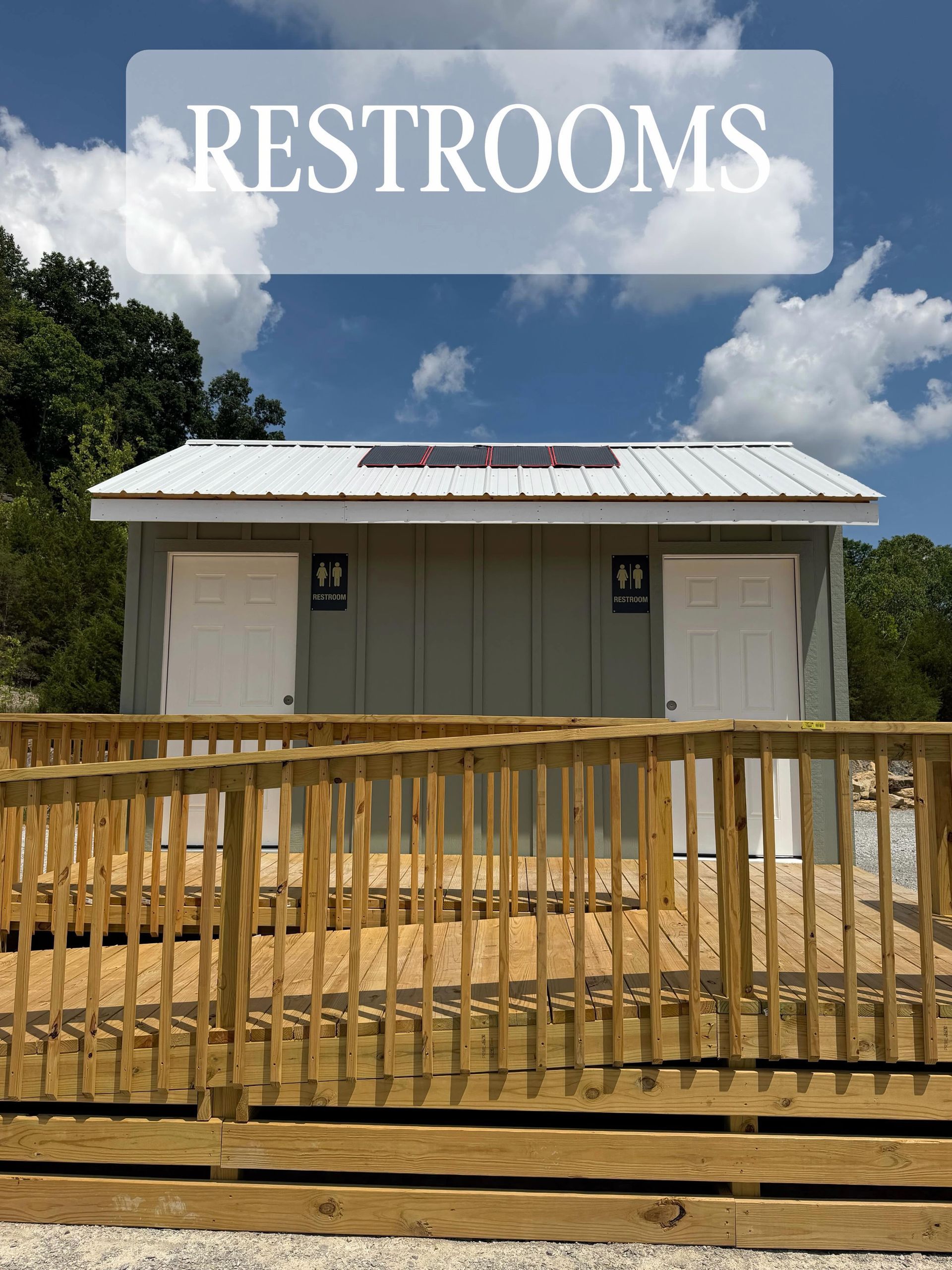 Restroom building with white roof and wooden fence under a blue sky with clouds