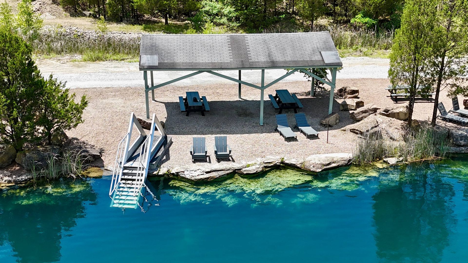 Lakeside dock with a shaded canopy, lounge chairs, and stairs leading into clear blue water.
