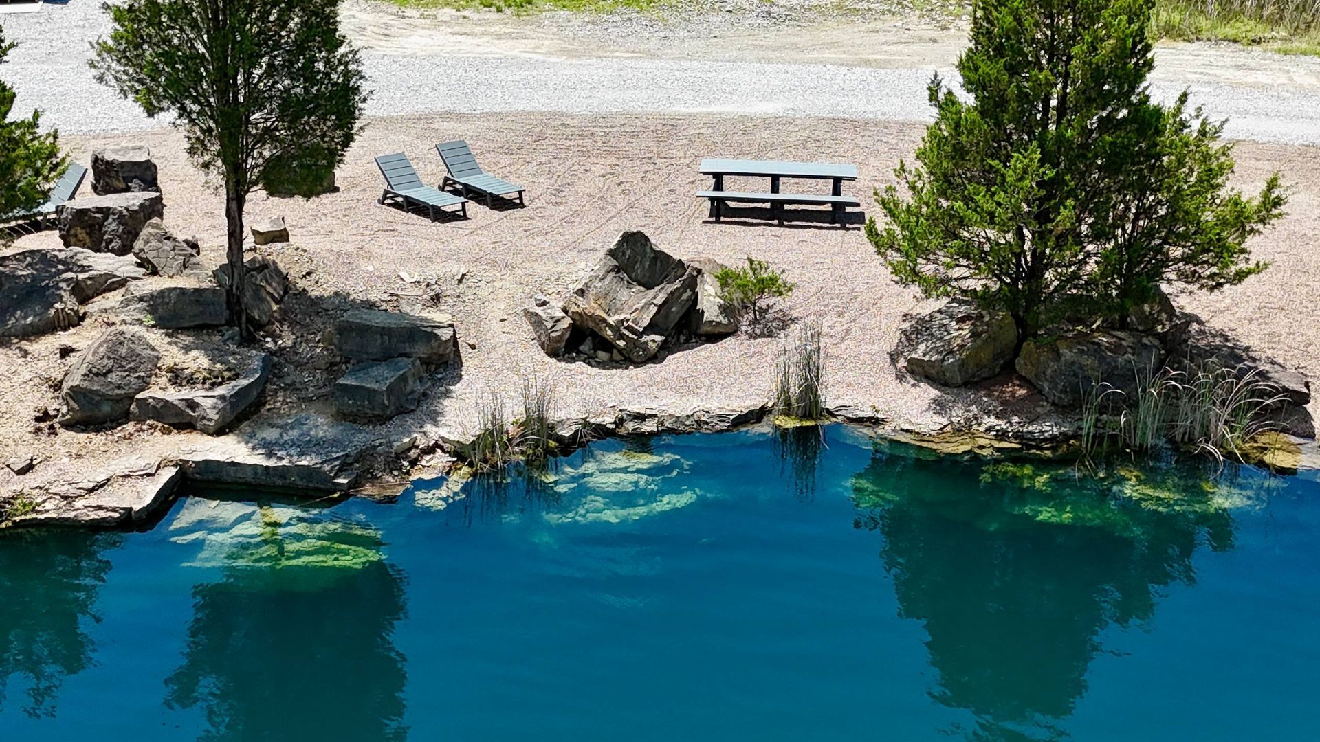 Rocky lakeshore with turquoise water, lounge chairs, picnic table, and trees.