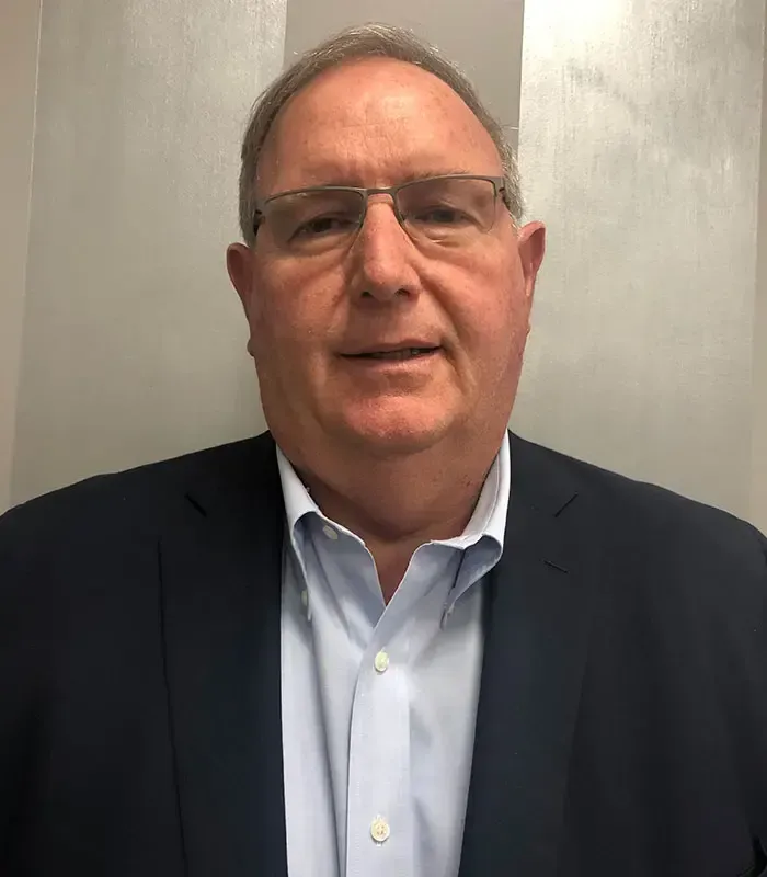 Man with glasses wearing a blue shirt and navy blazer smiles at the camera.