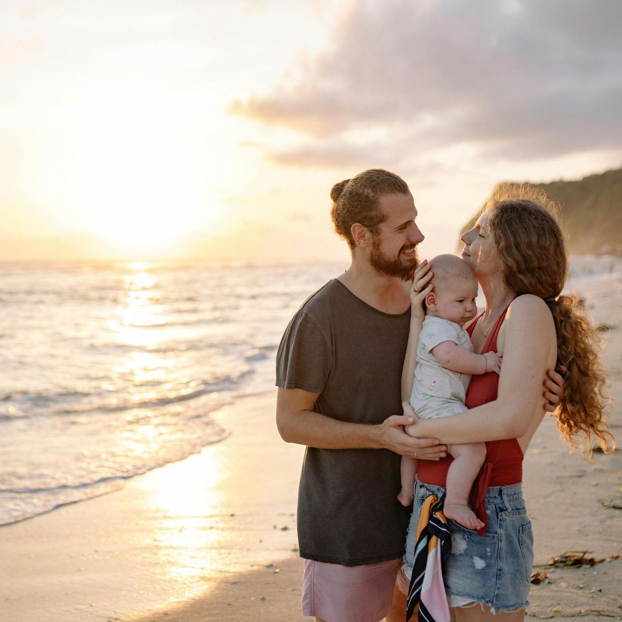 A man and woman are holding a baby on the beach.