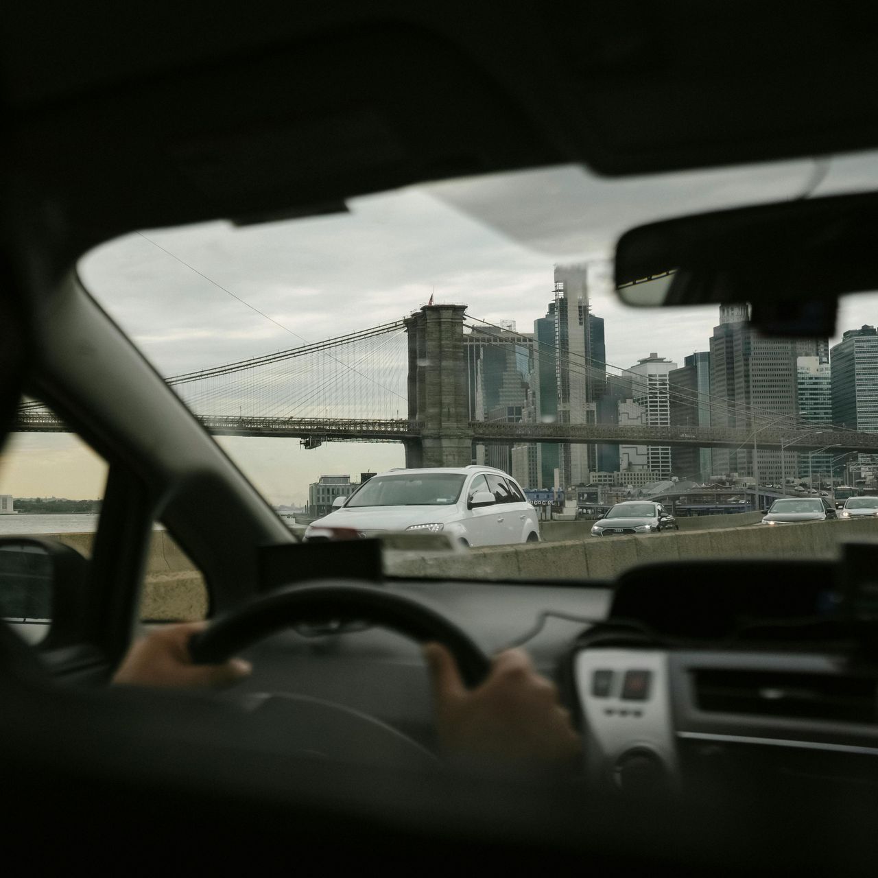 A person driving a car on a highway with a bridge in the background