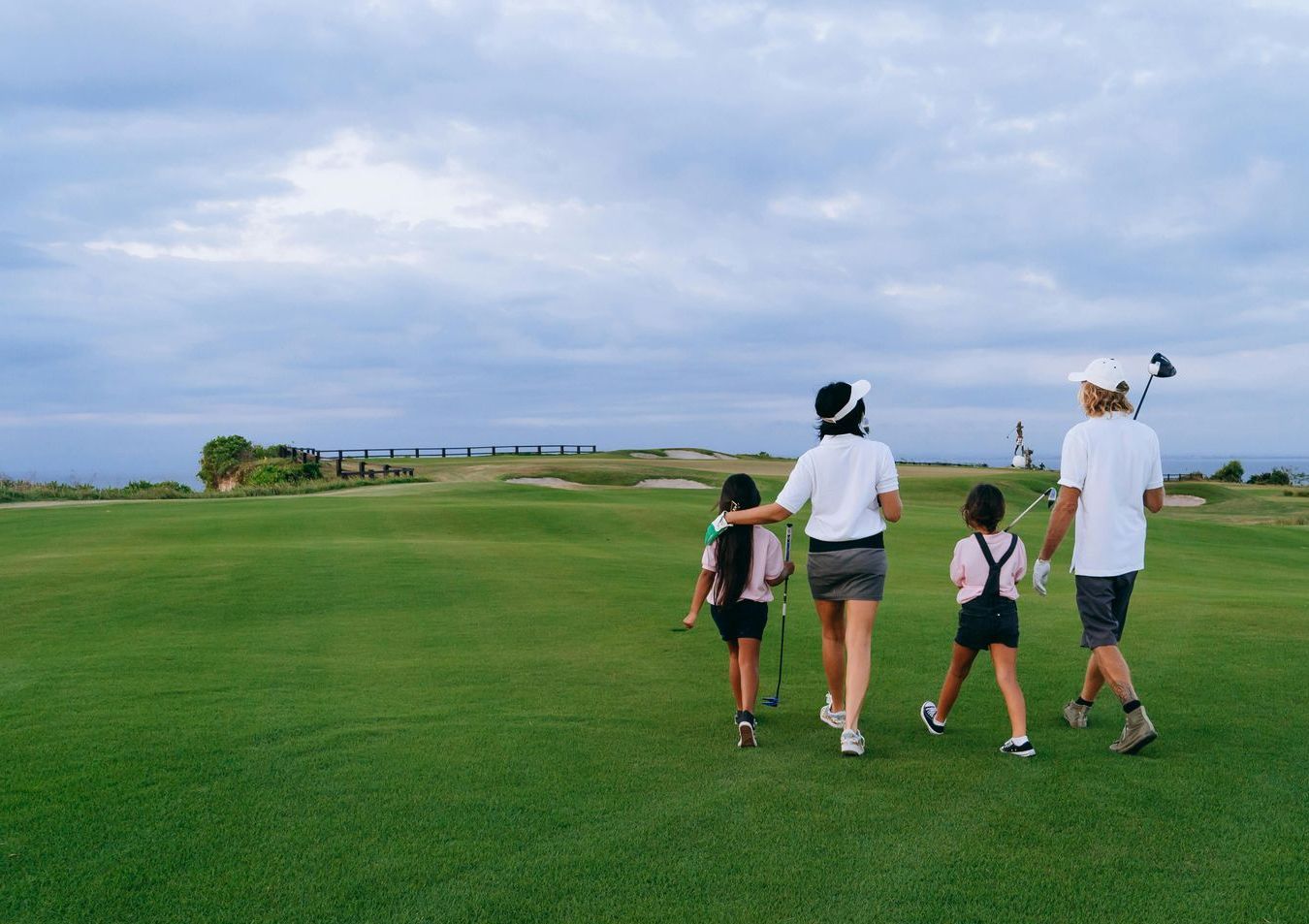 A family is walking across a golf course holding golf clubs.
