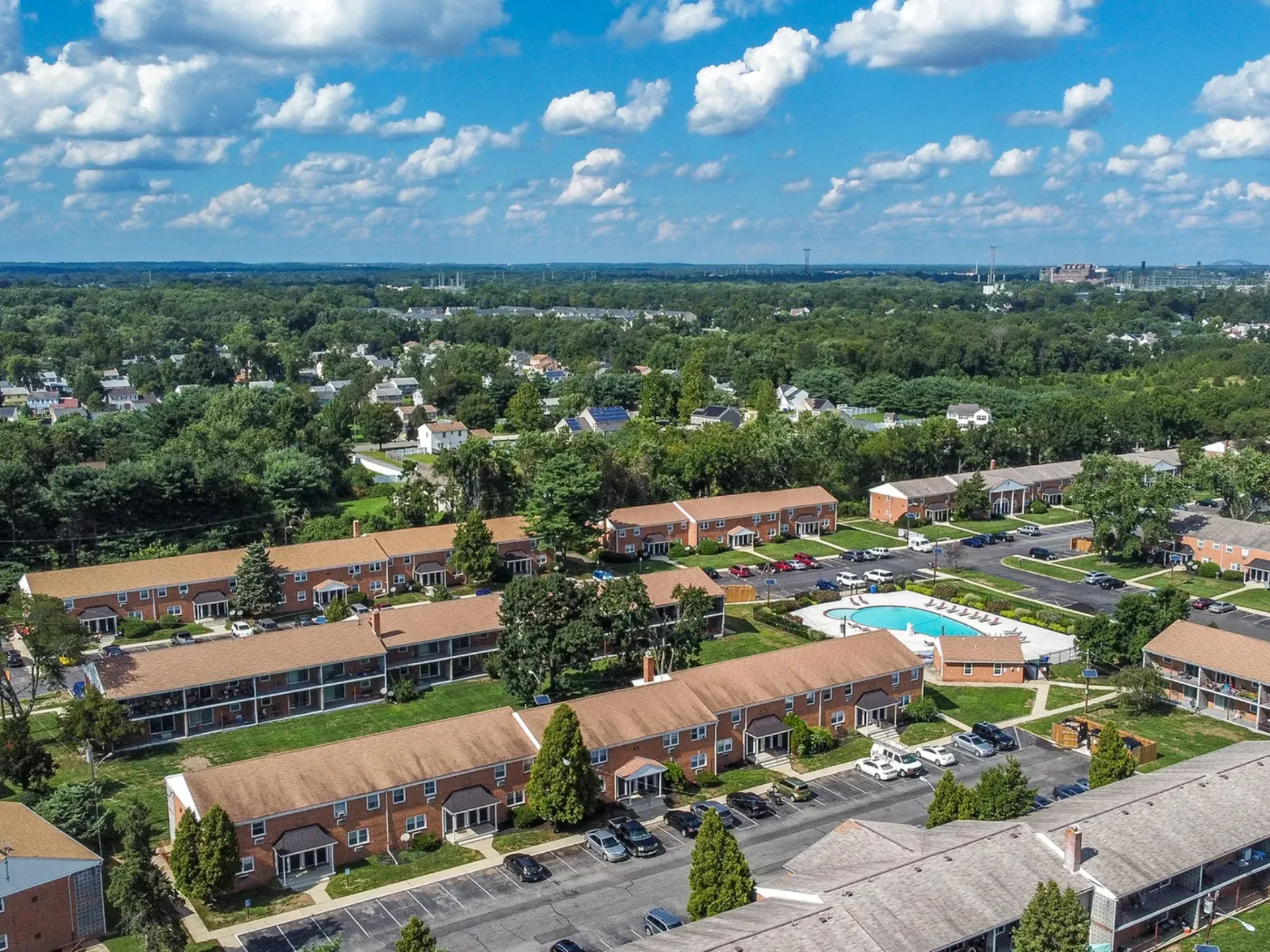 Aerial view of a brick apartment community with a central pool, parking, and surrounding trees.