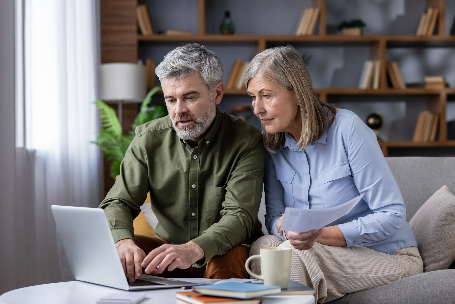 Mature couple on sofa using laptop and papers to review bills, budget and retirement plans. Mature couple on sofa using laptop and papers to review bills, budget and retirement plans.