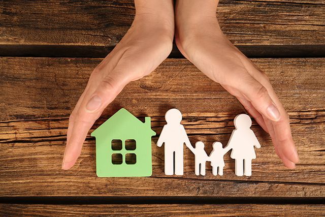 A pair of hands holds a cutout of a family next to a house, showing a concept for estate planning. A pair of hands holds a cutout of a family next to a house, showing a concept for estate planning.