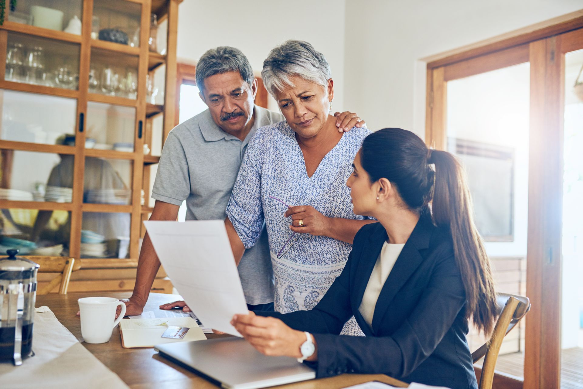 Estate planner reviews documents with a couple gathered around a table in a bright home office. Estate planner reviews documents with a couple gathered around a table in a bright home office.