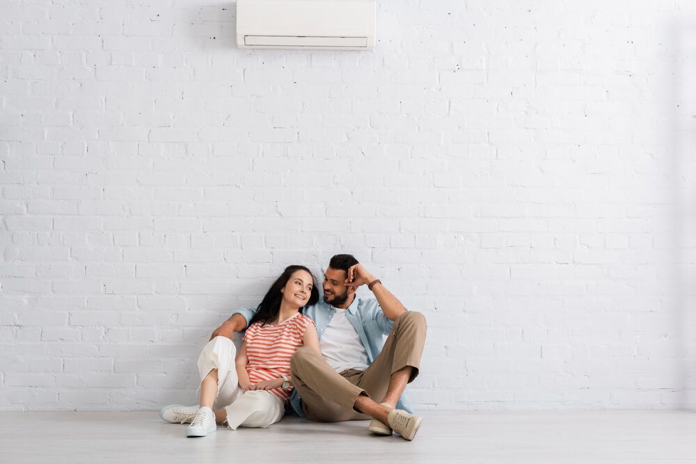 Couple Sitting Under Air Conditioner — HVAC Systems in Dubbo, NSW