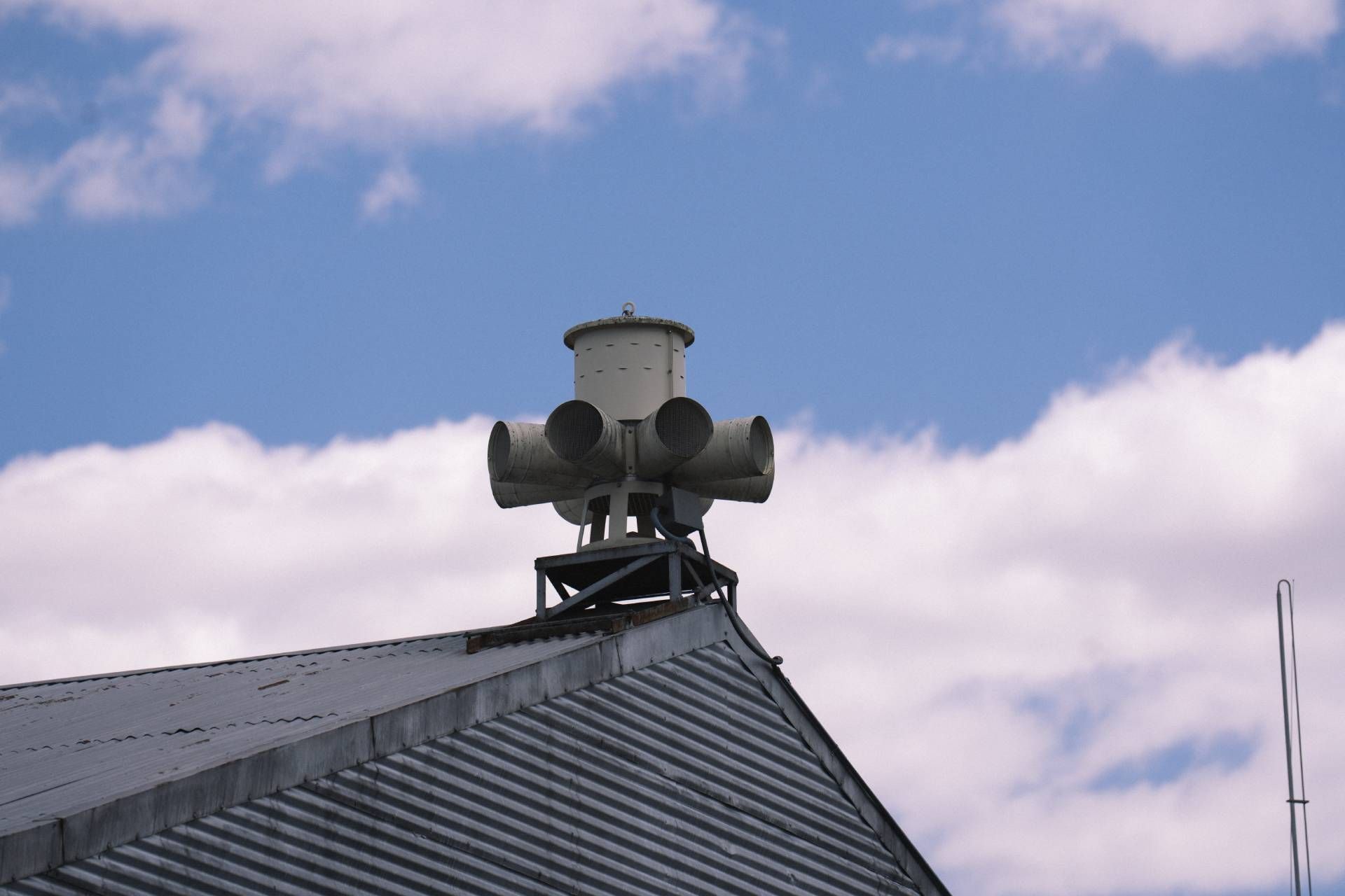 Rooftop warning siren on a metal roof against a blue sky with clouds