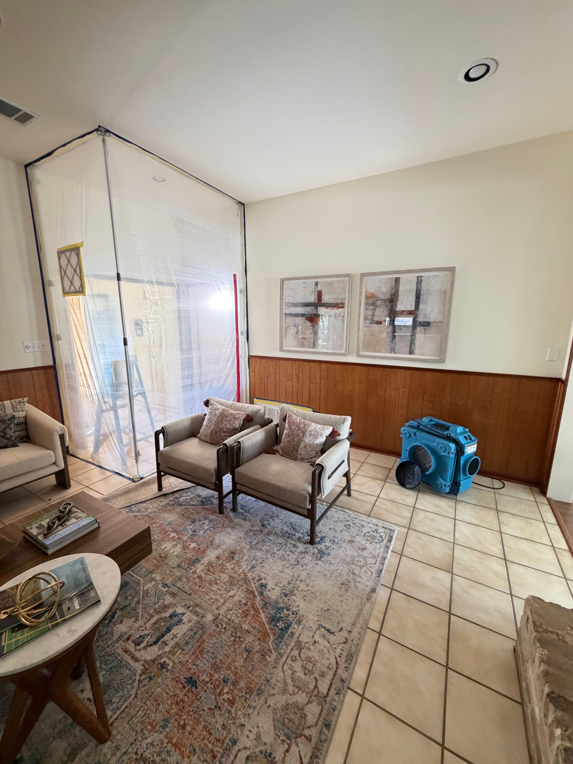 Living room with sofa, armchairs, patterned rug, tiled floor, and wood-paneled wall with framed art.