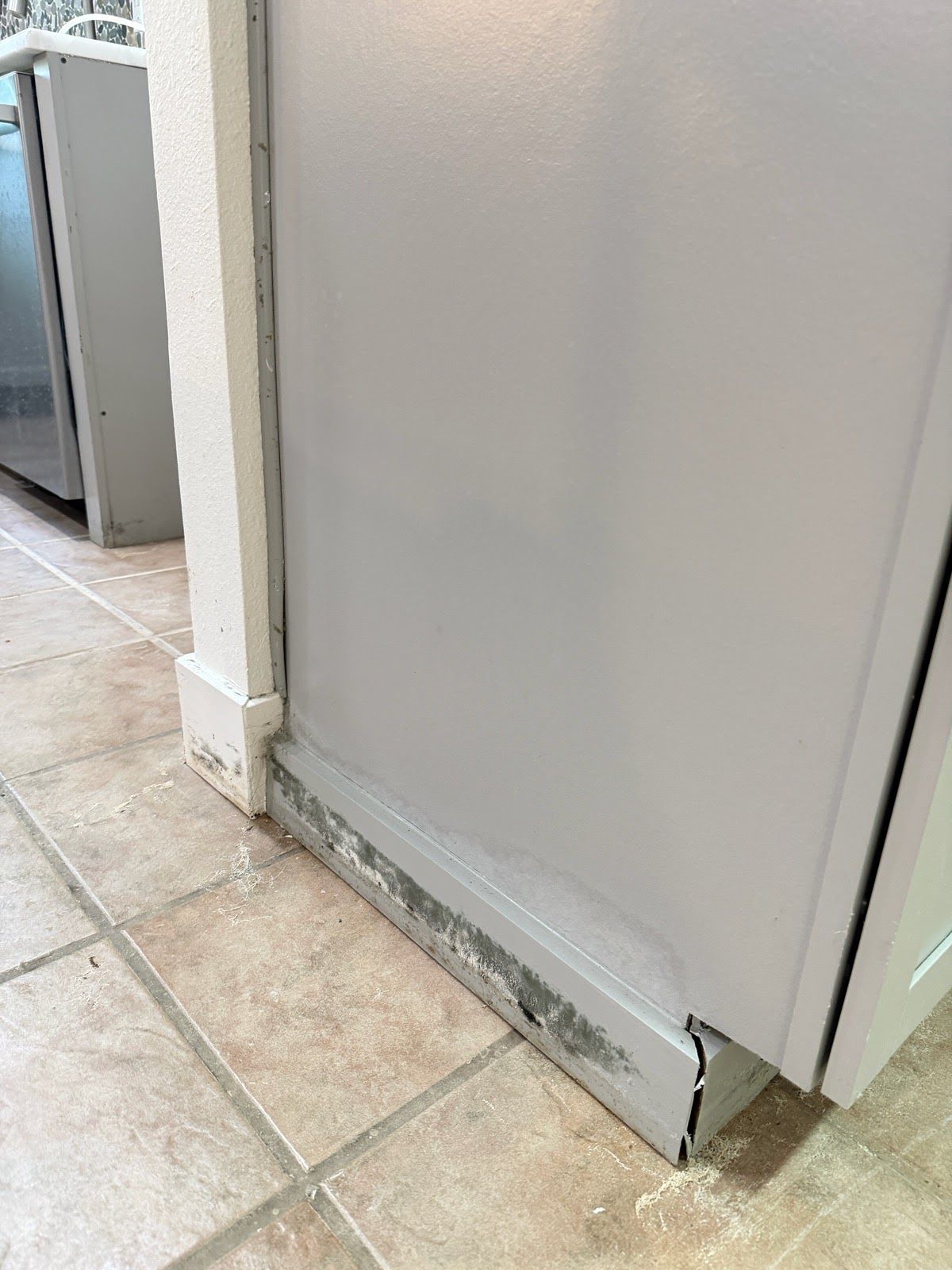 Damaged white wall baseboard and chipped corner beside tiled floor in a kitchen.