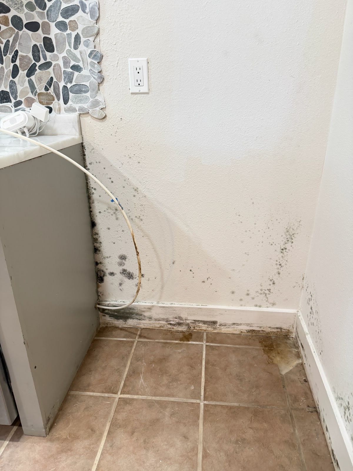 Small tiled corner with wall damage, mold stains, and a nearby cabinet edge.