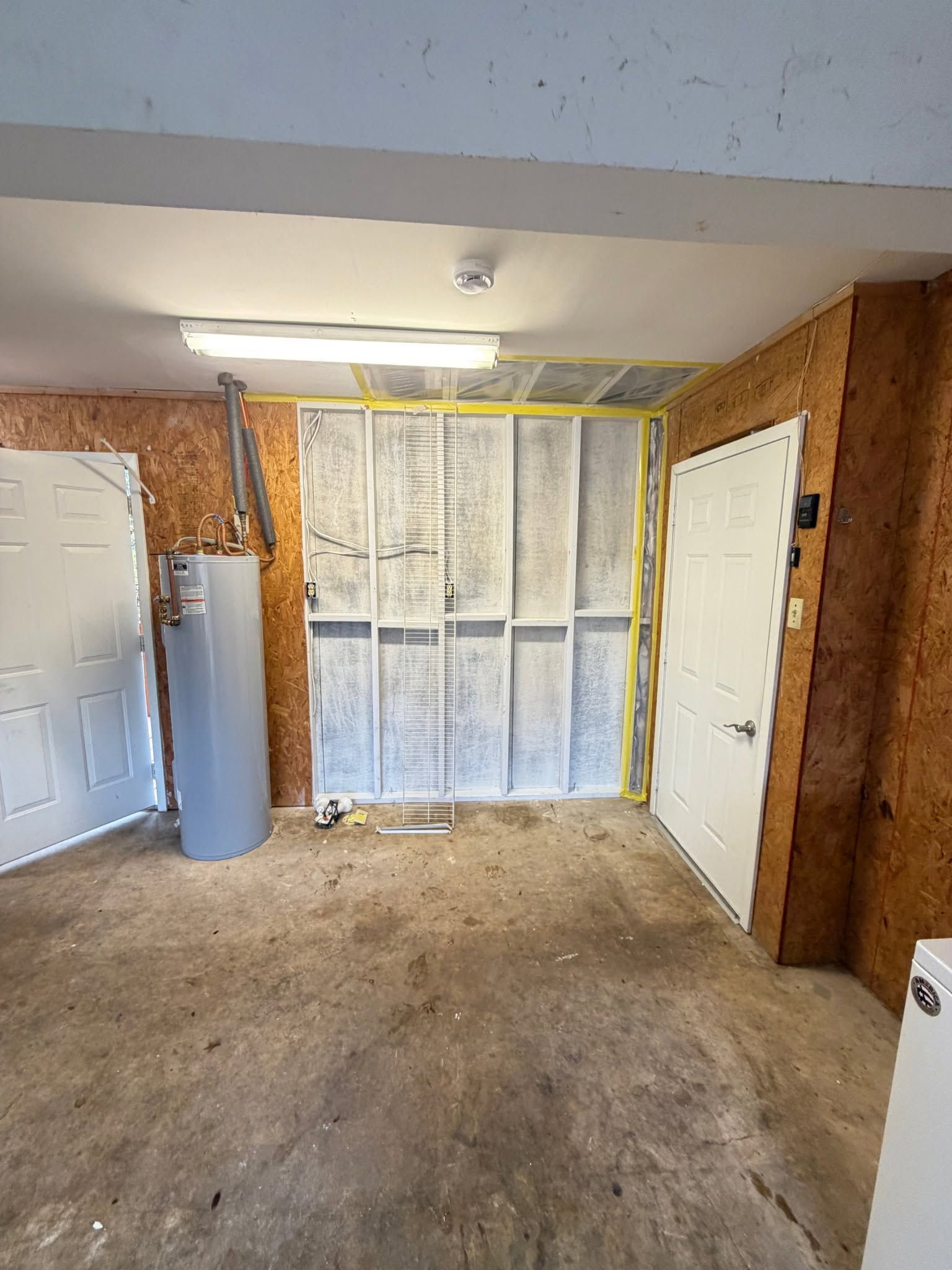 Empty garage with bare walls, central window covered in paper, white doors, and a fluorescent ceiling light.